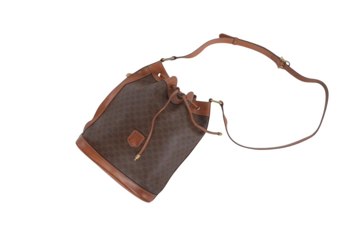 A brown monogram bucket bag with tan leather trim and a matching shoulder strap, shown on a plain white background.